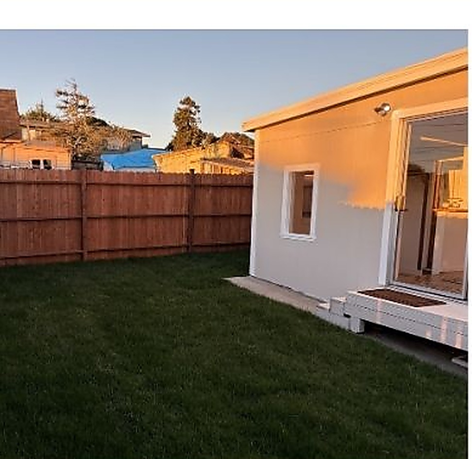 Backyard exterior at golden hour with a new lawn, cedar fencing, and sliding glass doors